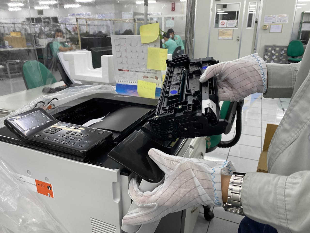 Worker replacing printer ink cartridge in a laboratory environment, highlighting technology maintenance.